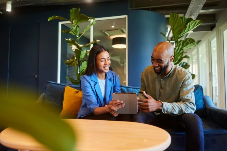 Smiling financial coach and client reviewing a digital plan on a tablet in a modern office, symbolizing collaborative money management and trust